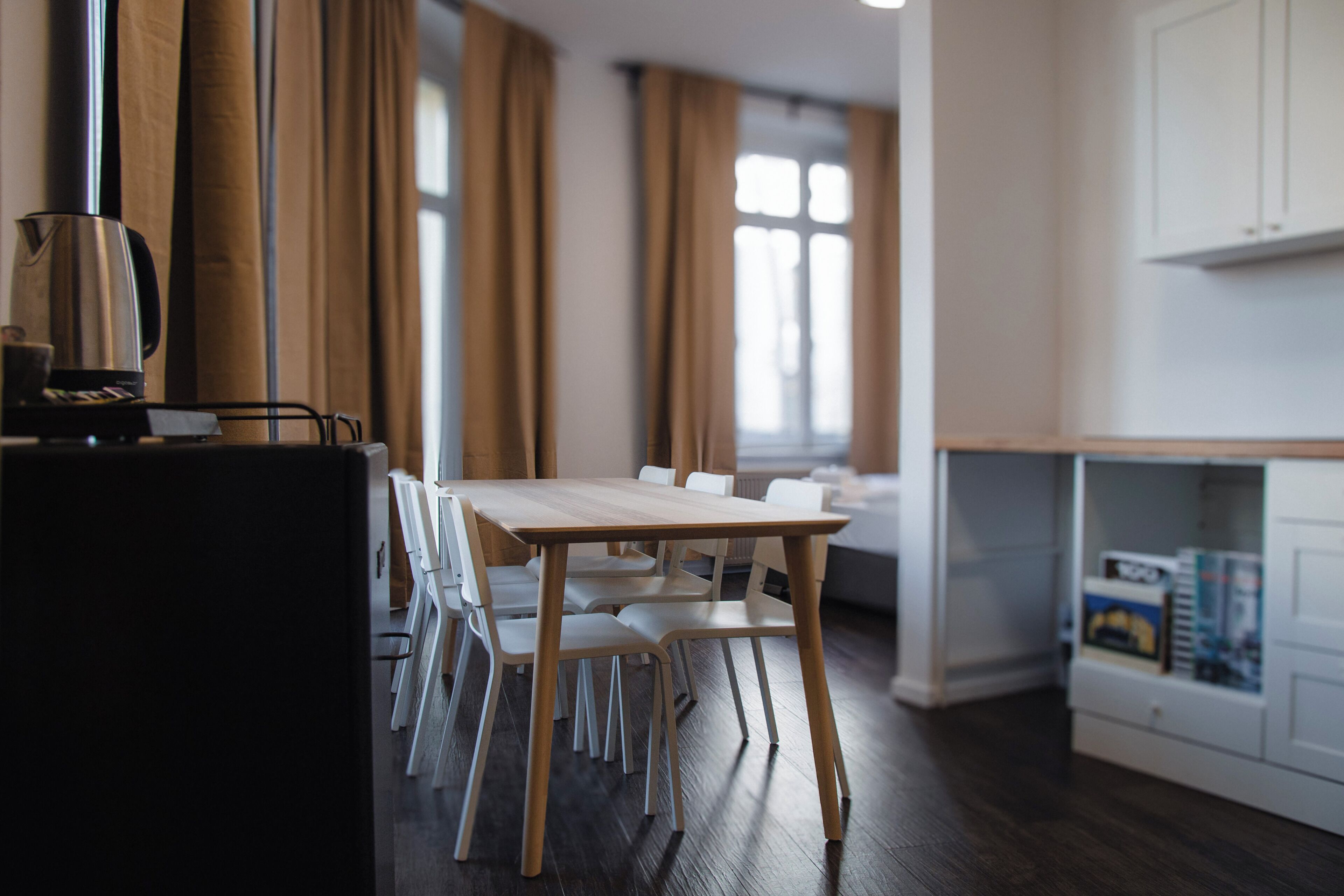 A modern kitchen with a wooden table and chairs, a coffee machine, and a white cabinet with storage.