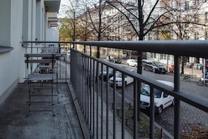 Un balcón con barandilla de metal que da a una calle con coches y bicicletas estacionados.