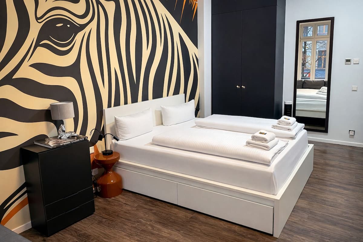 A modern bedroom with a large zebra mural, a double bed, a nightstand, and a mirror reflecting the room.