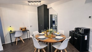 Un espace repas moderne avec une table ronde, des chaises blanches, un meuble noir et un petit coin cuisine équipé d’un four à micro-ondes et d’un réfrigérateur.