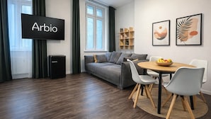 Un salon moderne avec un canapé, une table à manger, des chaises, un téléviseur et des œuvres d’art accrochées au mur.