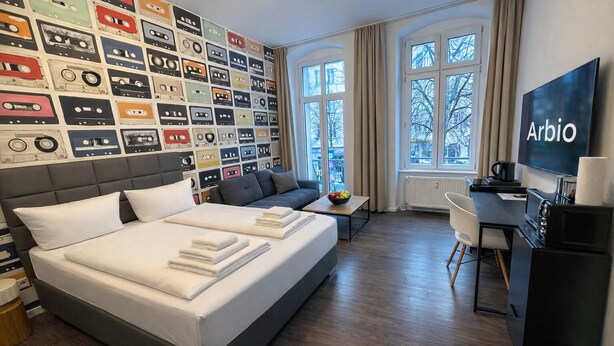 Une chambre d’hôtel avec un lit, un bureau, une télévision et un mur décoré de cassettes audio.