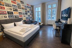 A hotel room with a bed, a desk, a TV, and a wall decorated with cassette tapes. - Arbio I Apartmently (Berlin)