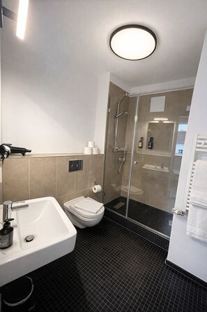 Un baño moderno con ducha de mampara de vidrio, lavamanos blanco y retrete.