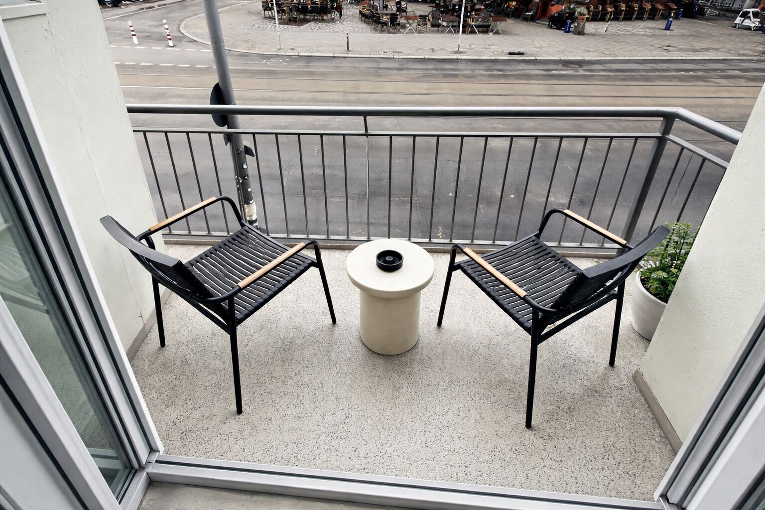 A balcony with two chairs and a table, a railing, and a view of the street.