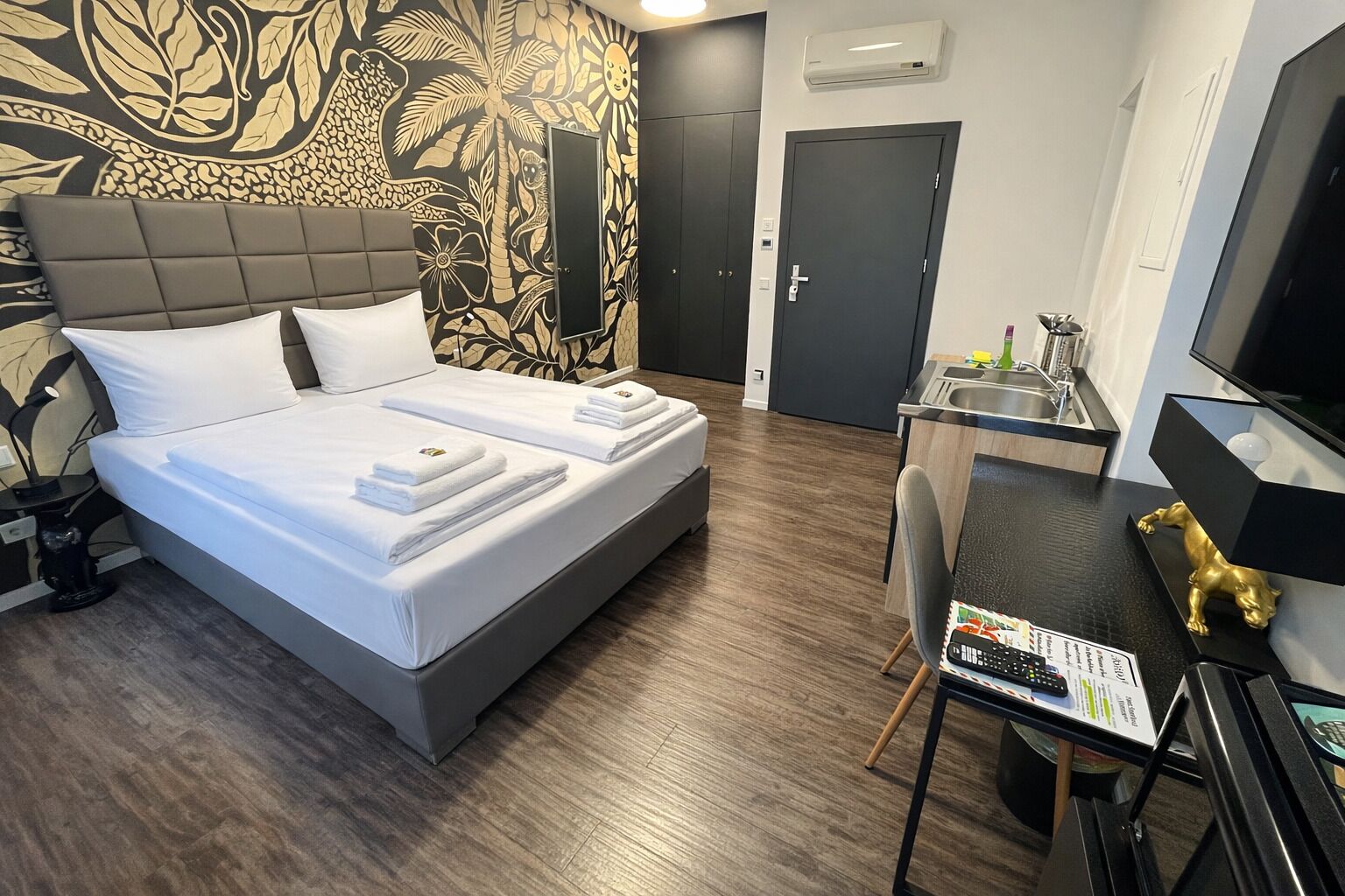 A hotel room with a bed, a desk, a chair, a TV, and a bathroom door.