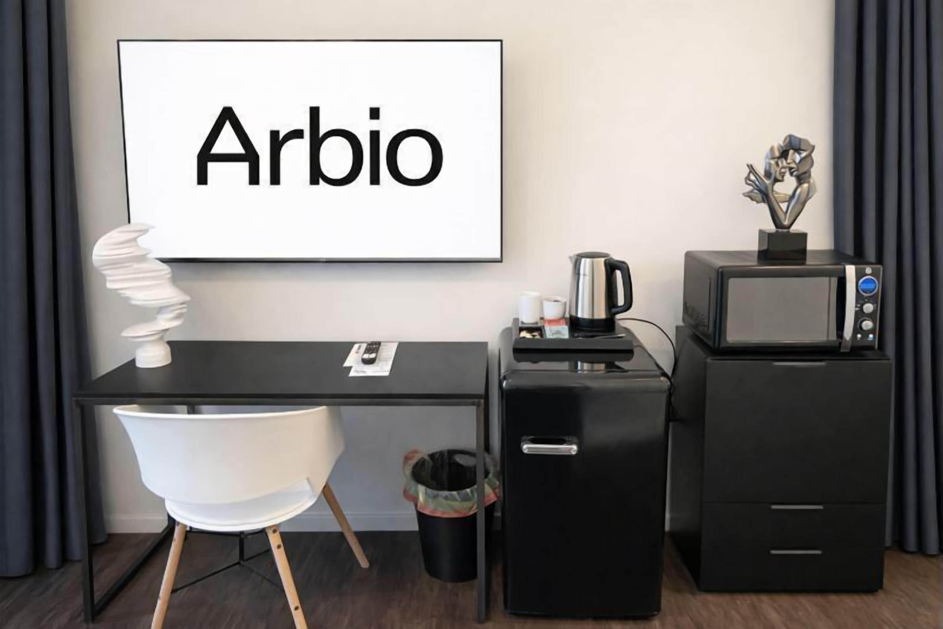 Een moderne kamer met een bureau, stoel, koffiezetapparaat, magnetron en een prullenbak.