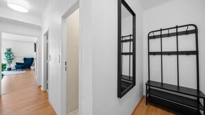 Un couloir avec un présentoir en métal noir, un grand miroir et une chaise bleue à l’arrière-plan.