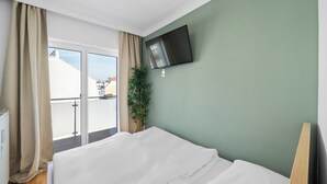 Une chambre d’hôtel avec un lit, un téléviseur fixé au mur, une plante et une vue sur la ville par la fenêtre.