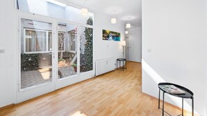 Un couloir lumineux doté d’un plancher en bois, une porte vitrée donnant sur un espace extérieur et une petite table avec un magazine.