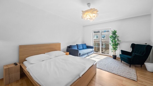 Une chambre moderne avec un lit en bois, un canapé bleu, un fauteuil foncé et une plante en pot.