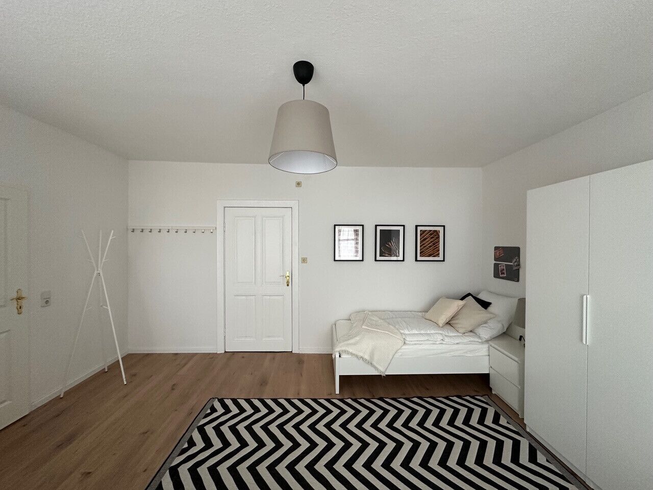 Un dormitorio con una cama, un armario blanco, una puerta y una lámpara colgante.