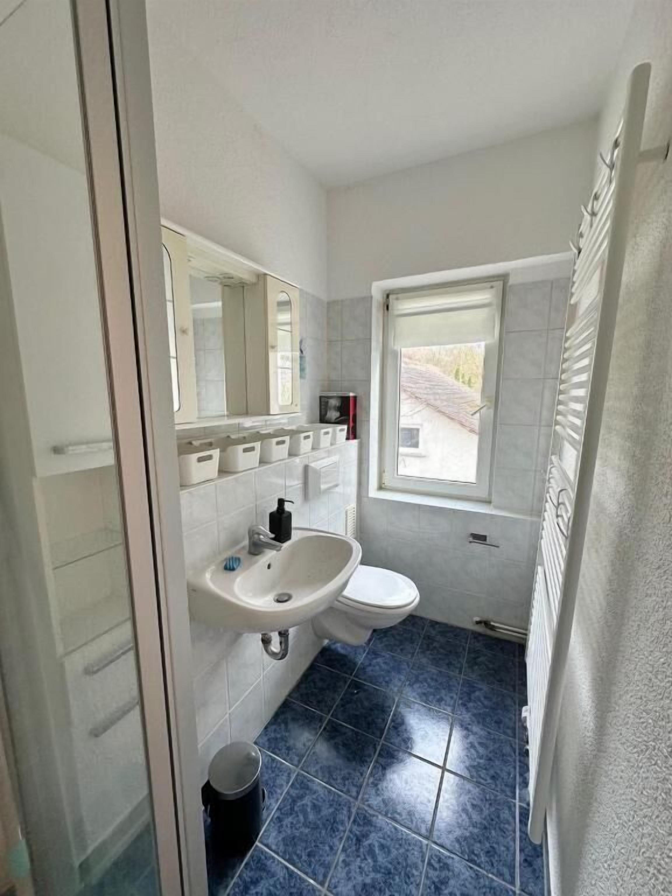 A bathroom with a white sink, mirror, and toilet. There is a window with a view of the outside.