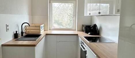 A compact kitchen with white cabinets, a wooden countertop, a window, and a built-in oven.