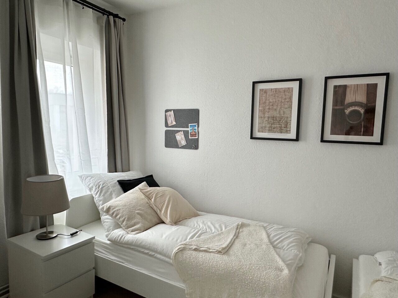 A minimalist bedroom with a bed, bedside table, and a wall-mounted bulletin board.