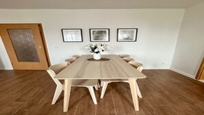 A dining room with a wooden table and chairs, a vase with flowers, and three framed pictures on the wall. - Arbio Monteurzimmer Tremmen (Ketzin/Havel)