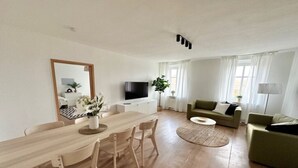 A modern living room with a wooden dining table, a sofa, and a TV. - Arbio Monteurzimmer Tremmen (Ketzin/Havel)