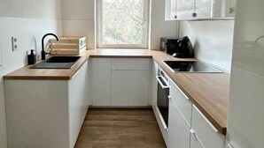 A compact kitchen with white cabinets, a wooden countertop, a window, and a built-in oven. - Arbio Monteurzimmer Tremmen (Ketzin/Havel)