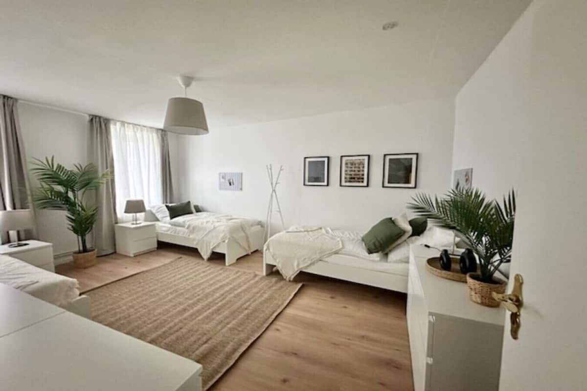 Une chambre à coucher moderne et minimaliste, avec un grand lit, des tables de chevet, une lampe sur pied et une plante en pot.