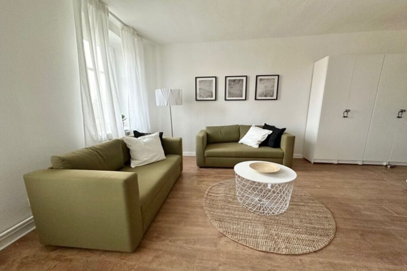 A living room with two green sofas, a round coffee table, and three framed pictures on the wall.