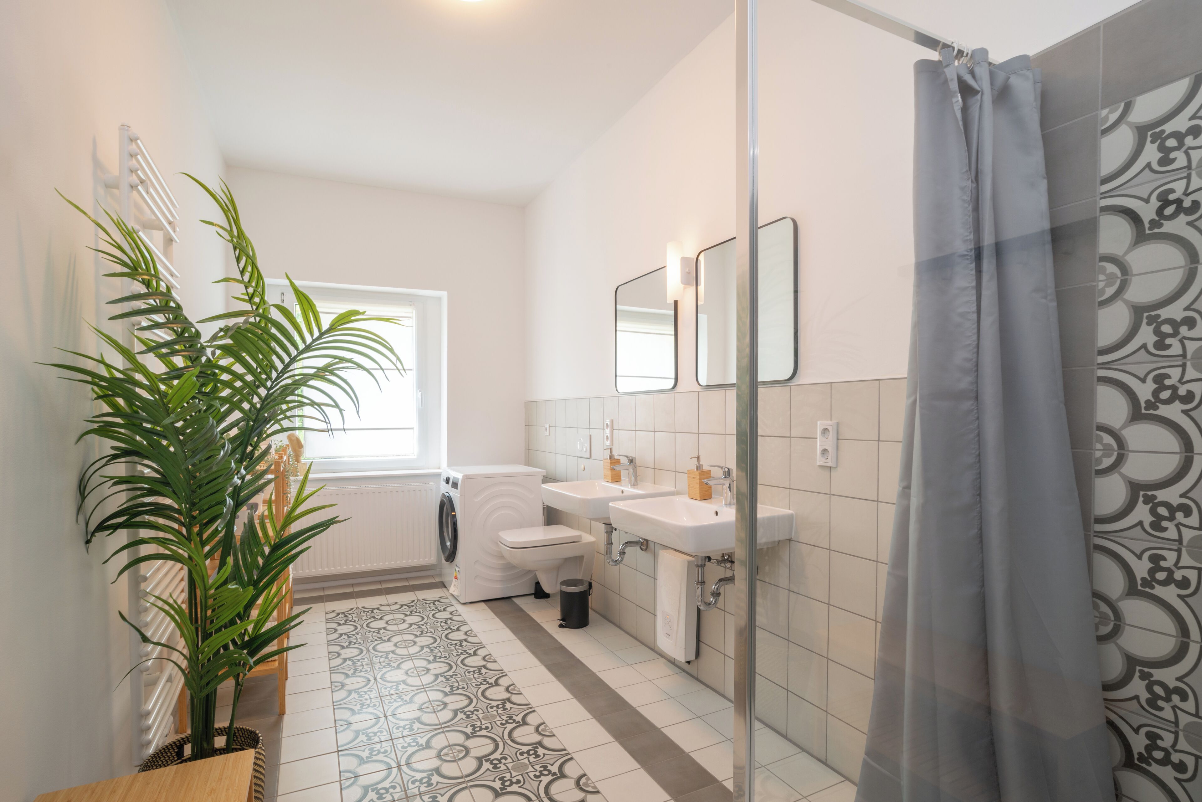 Un baño moderno con lavadora, dos lavamanos, inodoro y cortina de ducha.
