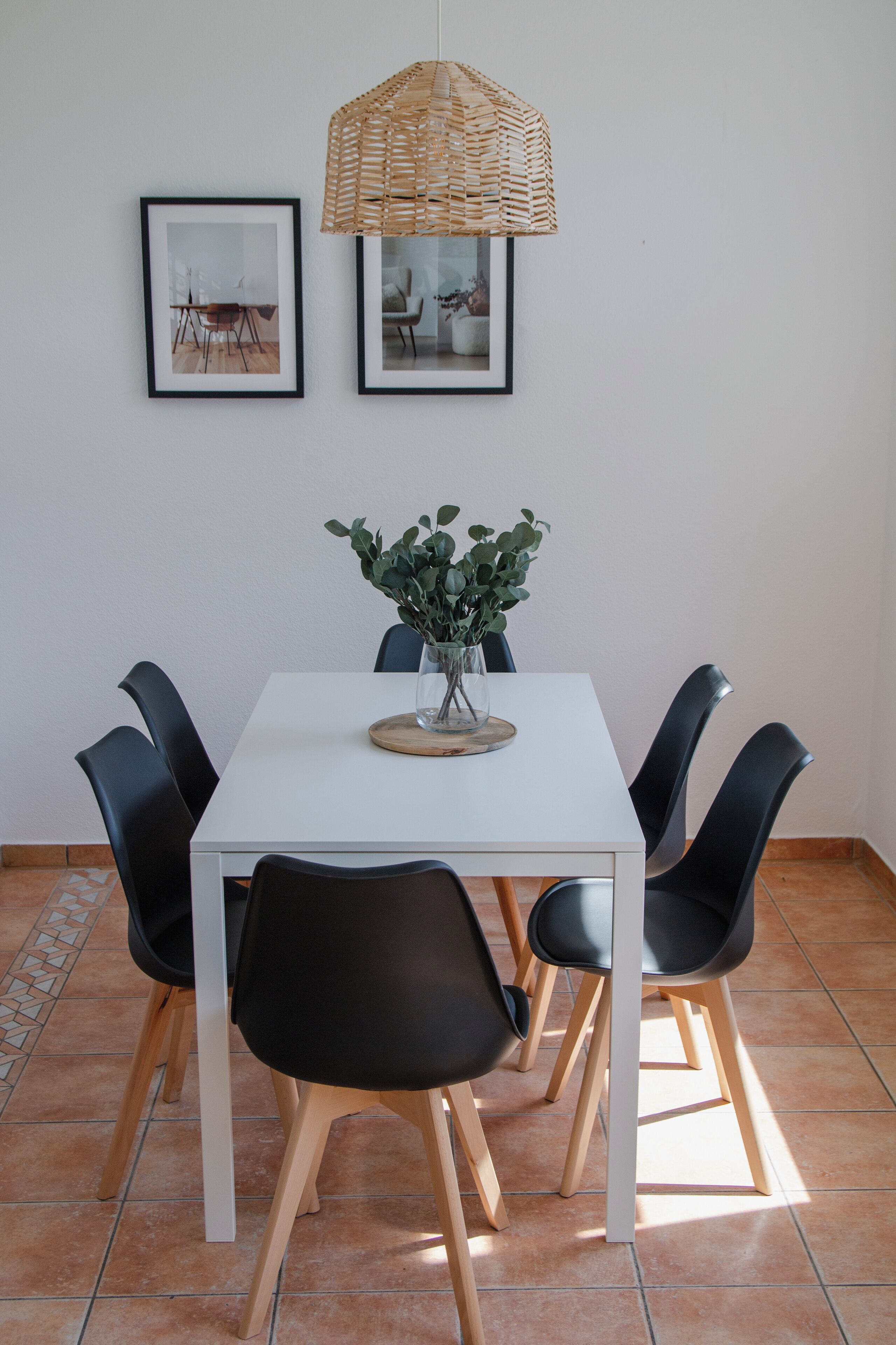 Ein Essbereich mit einem weißen Tisch, schwarzen Stühlen, einer Vase mit Grünpflanzen und zwei gerahmten Bildern an der Wand.