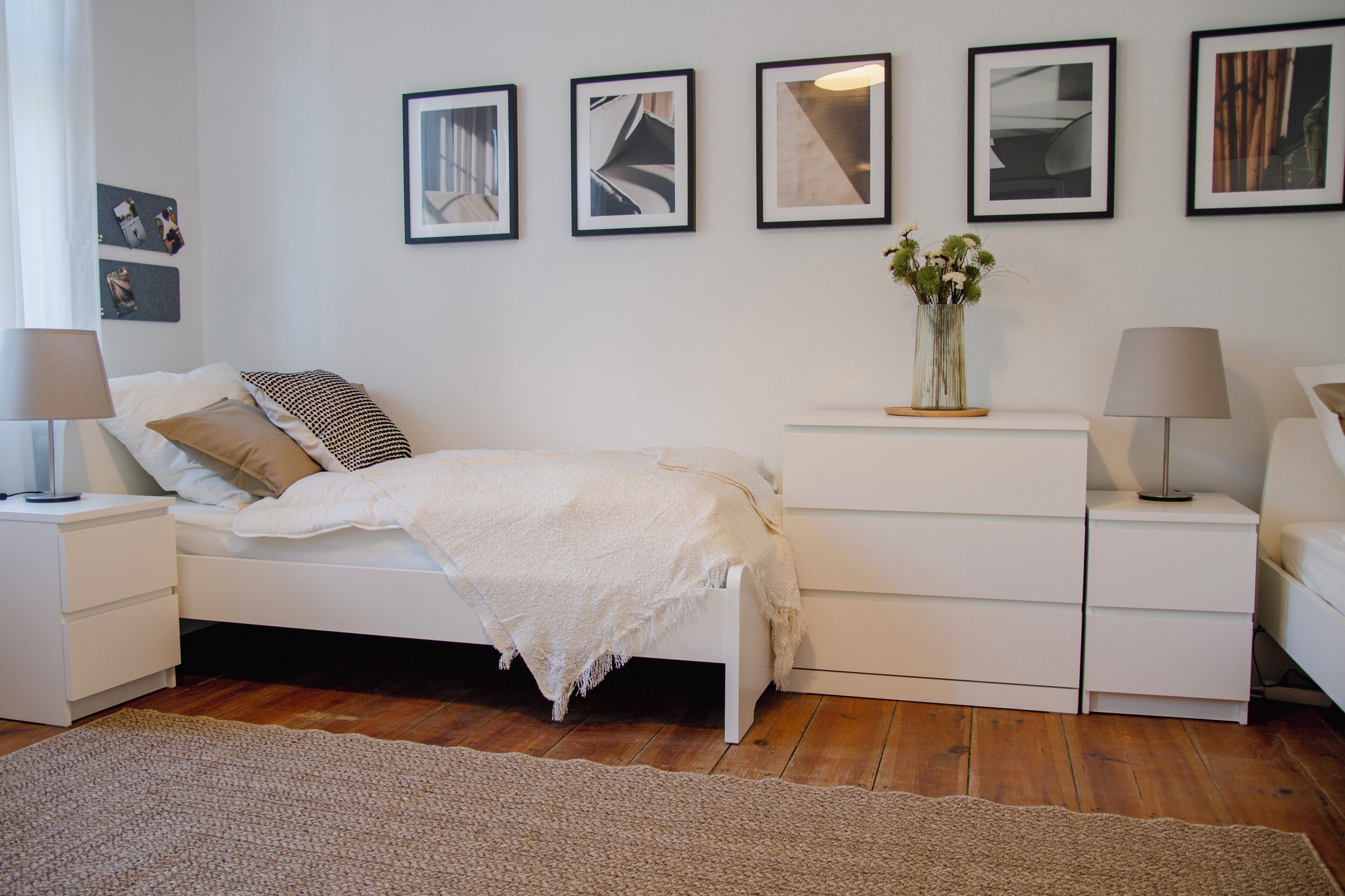 A modern bedroom with a white bed, bedside tables, a dresser, and a large rug.