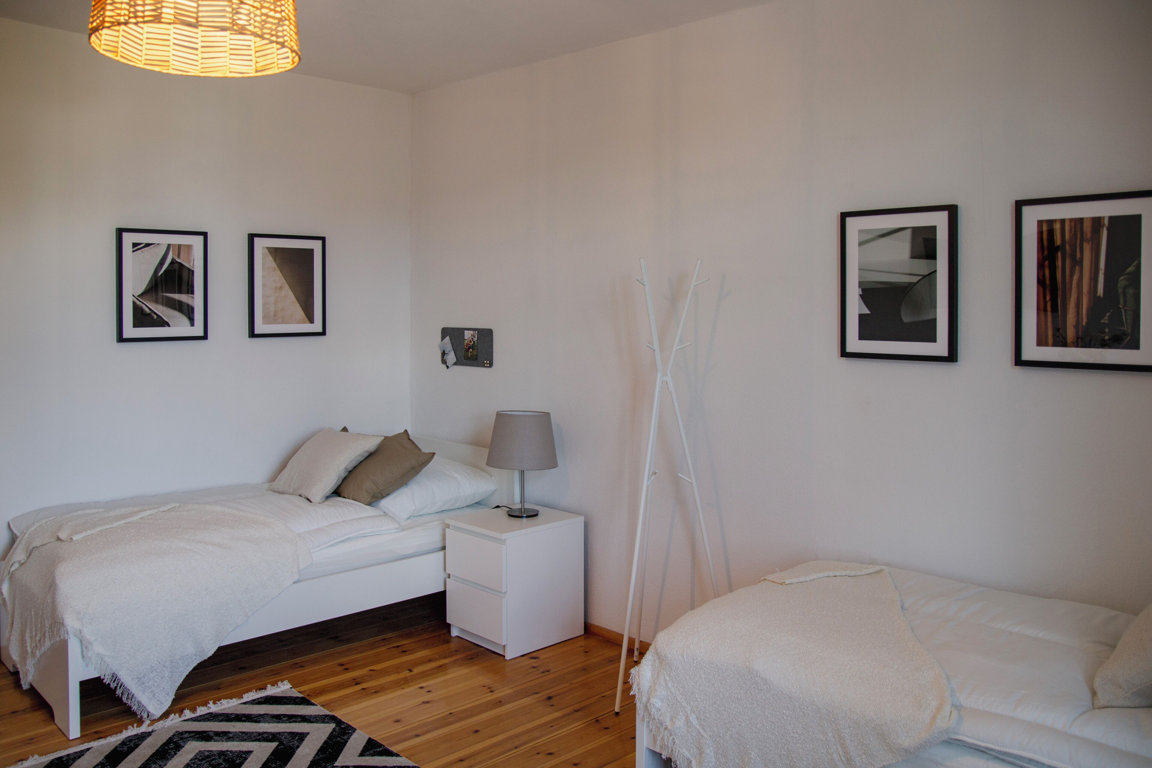 A bedroom with two beds, a bedside table with a lamp, and framed pictures on the wall.