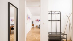 A hallway with a wooden floor, a black metal bench, a coat rack, and a mirror. - Anna And Friends (Graz)