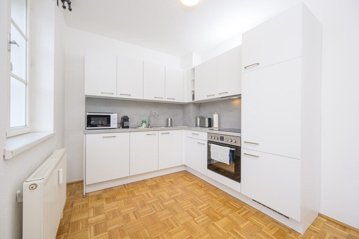 A compact kitchen with white cabinets, a microwave, a stove, and a window.