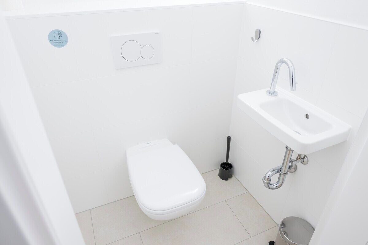 Un baño pequeño y blanco con inodoro, lavabo y escobilla.