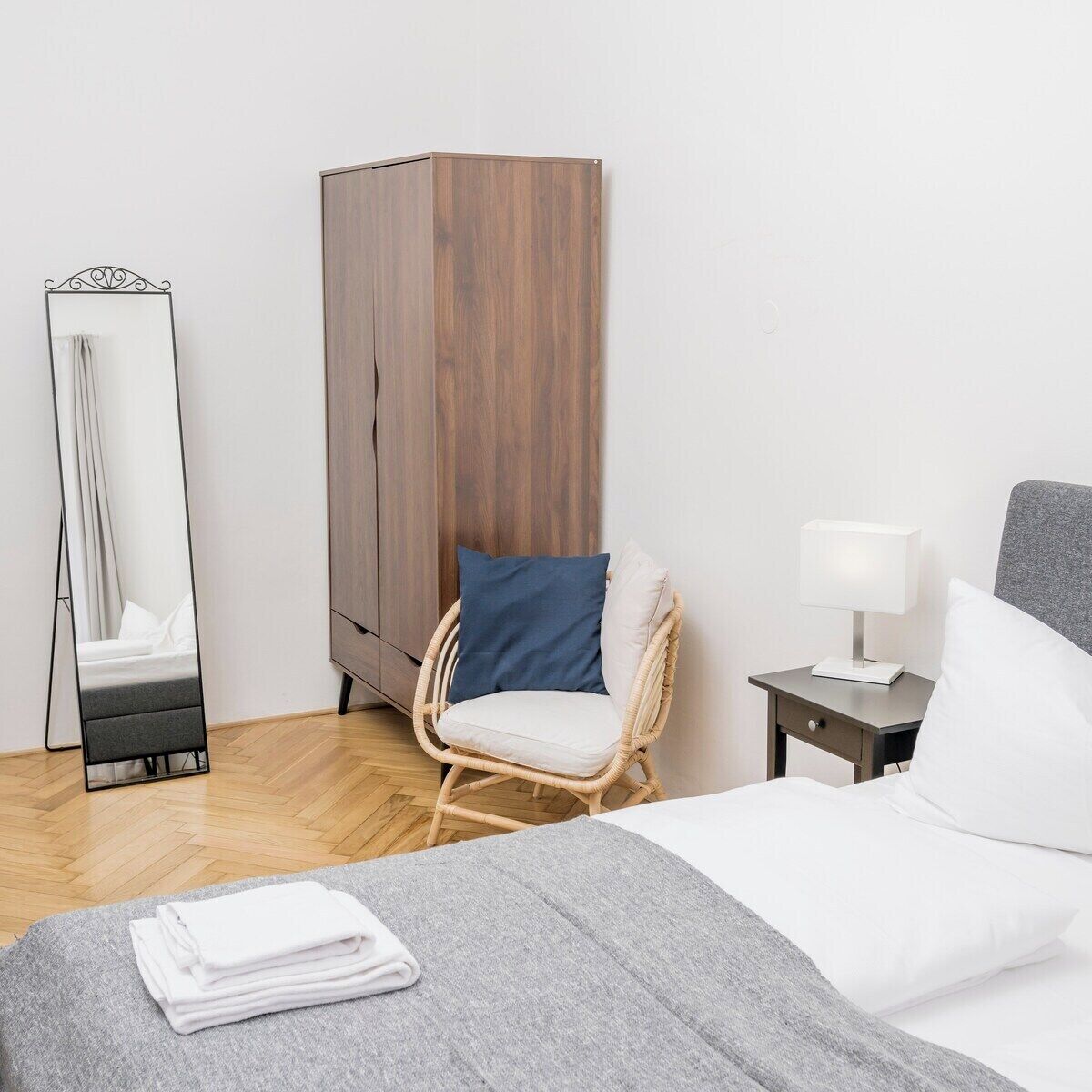 Una habitación de hotel con una cama, una silla, un armario, una mesita de noche y un espejo.