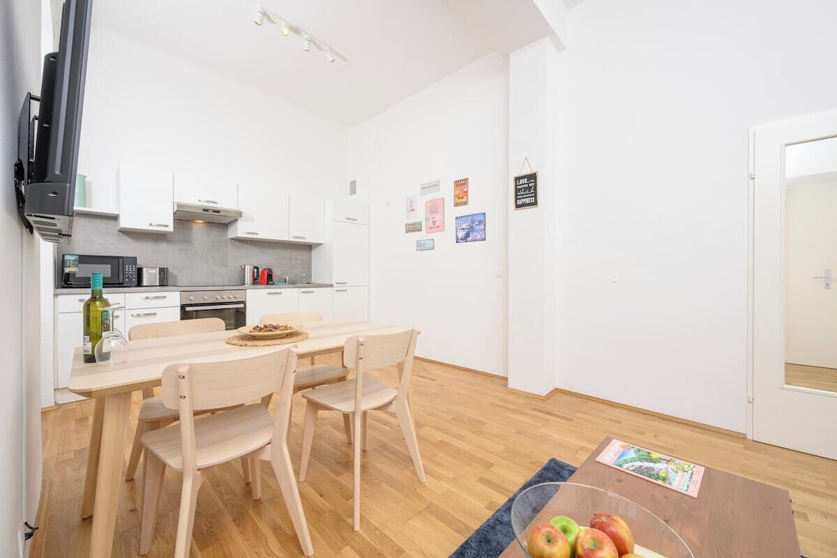 Una cocina moderna con armarios blancos, una mesa de comedor con sillas, un microondas y una cafetera.