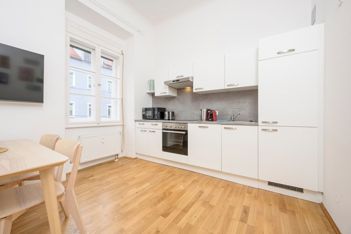 A modern kitchen with white cabinets, a built-in oven, and a coffee machine.
