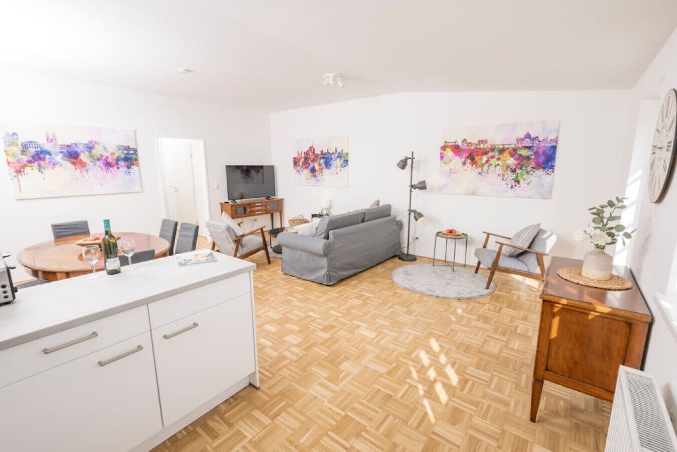 A modern living room with a grey sofa, a dining table with chairs, a TV, and artwork on the walls.
