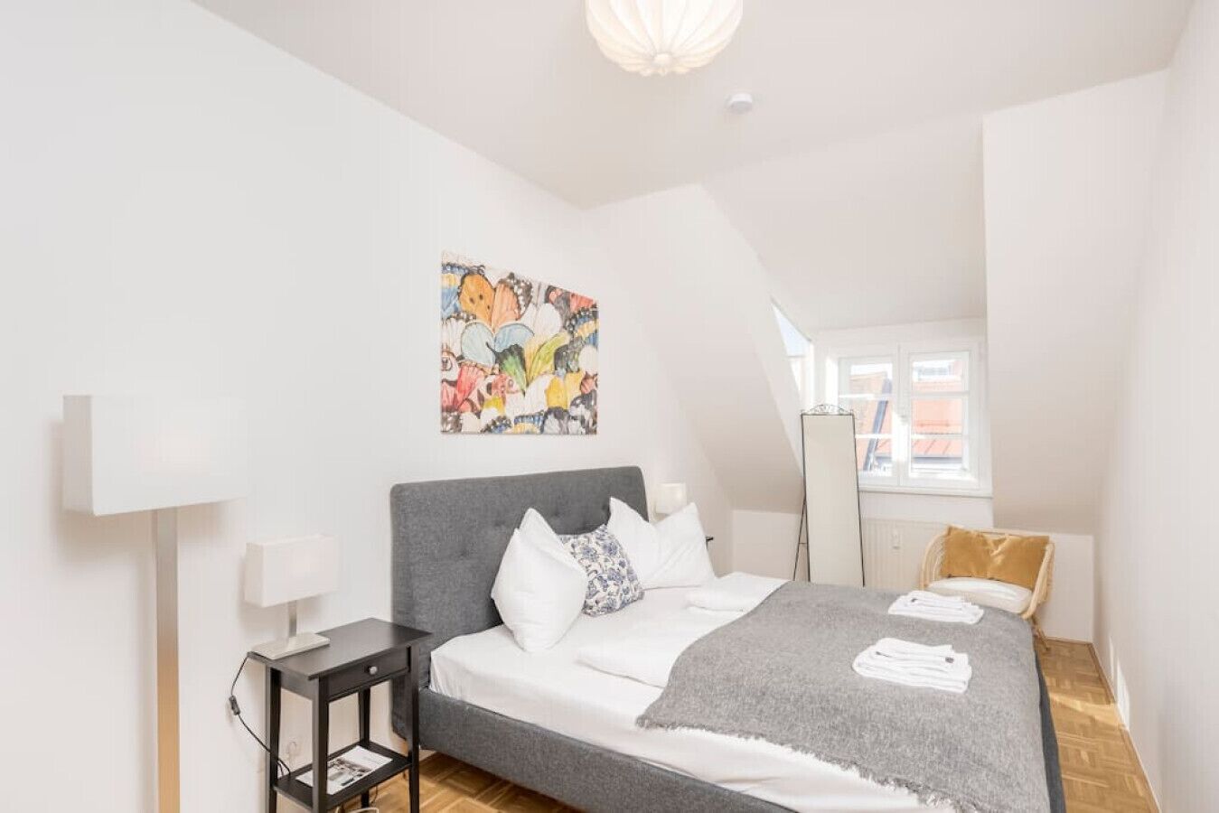 A modern bedroom with a grey bed, white pillows, and a colorful abstract painting on the wall.