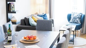 A modern dining area with a dark wooden table, grey upholstered chairs, and a fruit plate. A bottle of wine and glasses are on the table. - Anna And Friends (Graz)
