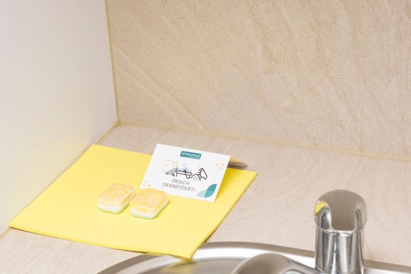 A kitchen sink with a yellow sponge and a cleaning card on a yellow cloth.