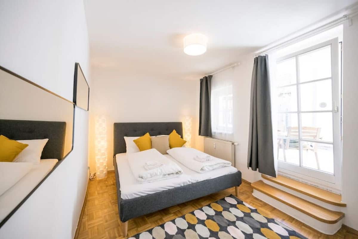 Ein modernes Hotelzimmer mit einem großen Bett, Holzboden, einem gemusterten Teppich und einem Fenster mit Vorhängen.