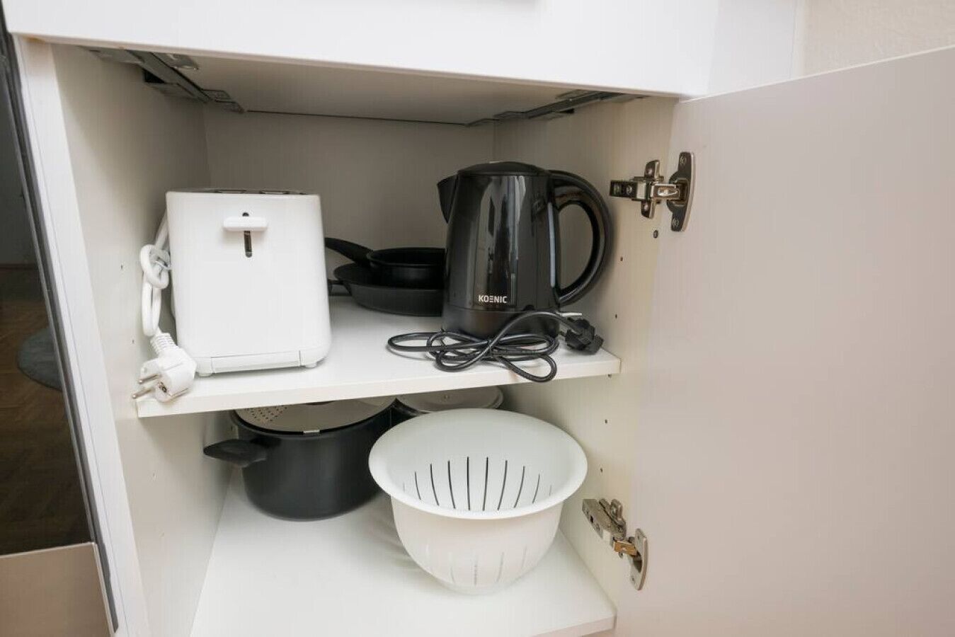 A kitchen with a white countertop, a coffee maker, a kettle, a white colander, and a power strip.
