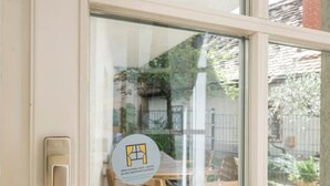 A window with a view of a wooden table and chairs outside, a door with a handle, and a glass pane reflecting the outside scene. - Zum Grazer Uhrturm (Graz)