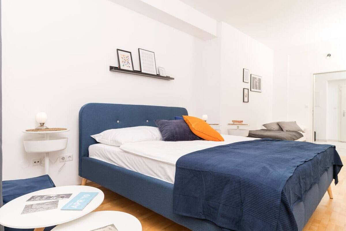 Ein modernes Schlafzimmer mit einem großen Bett, einem Nachttisch mit Lampe, einem kleinen runden Tisch und einer Wandablage mit Bildern.