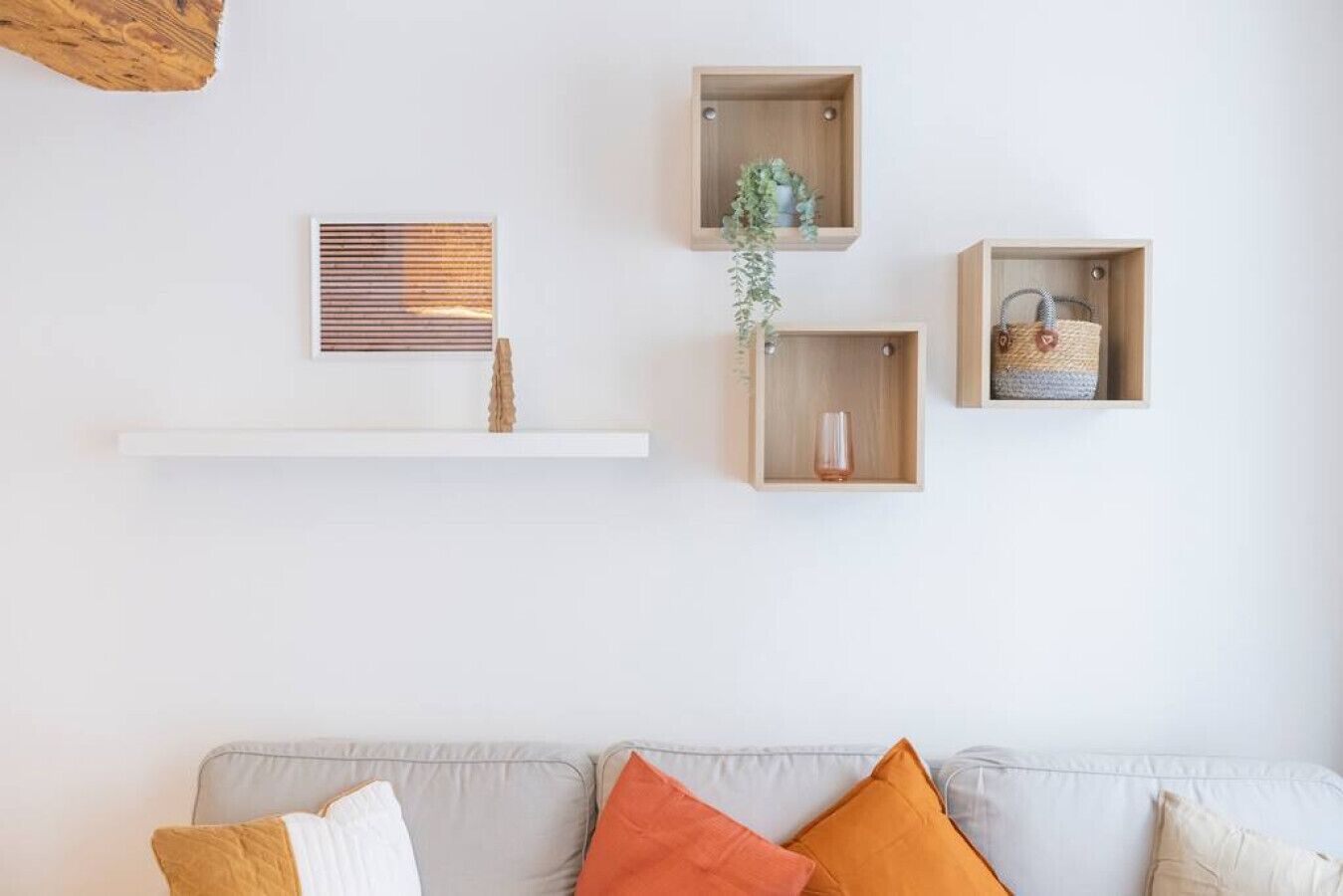 A living room with a white sofa, three wooden shelves, a framed artwork, and a hanging plant.
