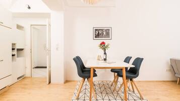 A modern kitchen with white cabinets and a wooden floor. There is a dining area with a table and chairs, and a picture on the wall.
