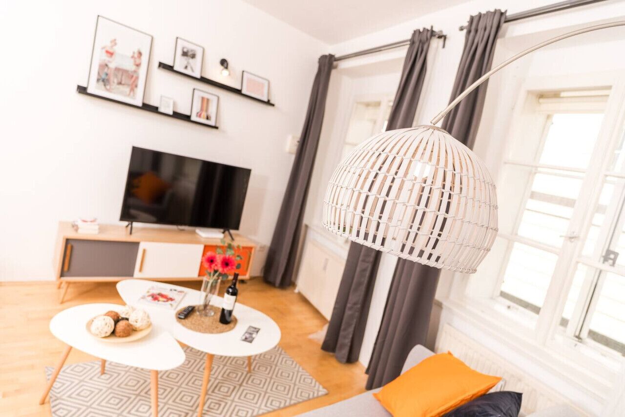 A modern living room with a TV, a dining table with a vase of flowers, and a unique hanging light fixture.