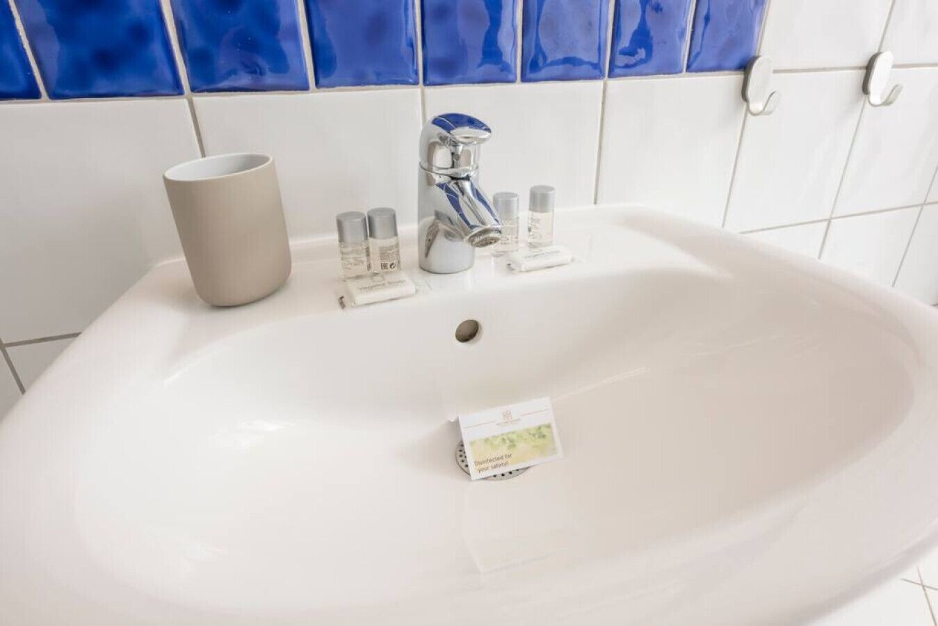 A white bathroom sink with a silver faucet, a beige cup, and several small bottles of toiletries.