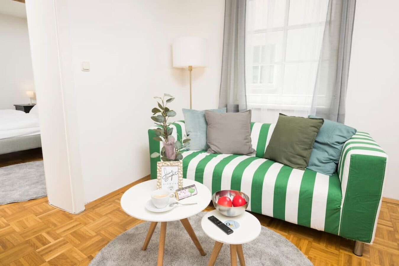 A green and white striped sofa with a remote control on a small table, a white lamp, and a framed picture on the table.