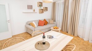 A modern living room with a sofa, dining table, and chairs. There is a hanging light fixture and a small side table with a basket of fruit. - Zum Grazer Uhrturm (Graz)