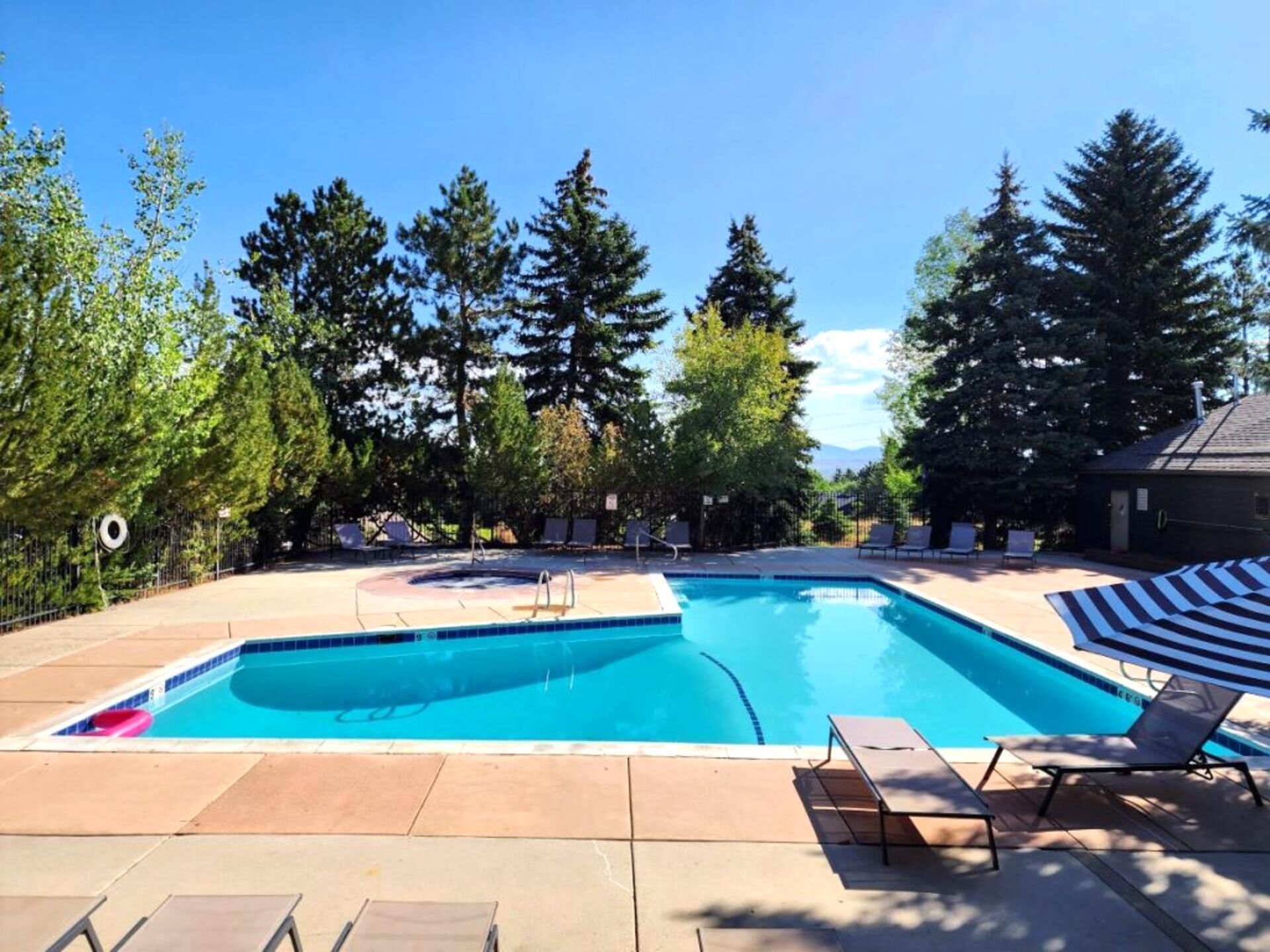A rectangular swimming pool with a diving board, surrounded by lounge chairs and trees.