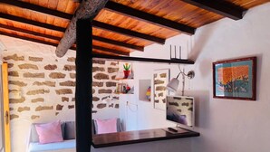A cozy room with a stone wall, wooden beams, a sofa, a small table, and a TV.
